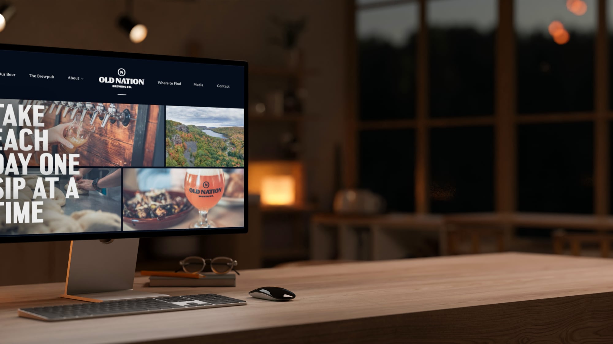 A desktop computer screen displays the Old Nation Brewing Co. website featuring beer and food photos. The monitor, keyboard, and mouse rest on a wooden desk in a dark interior.