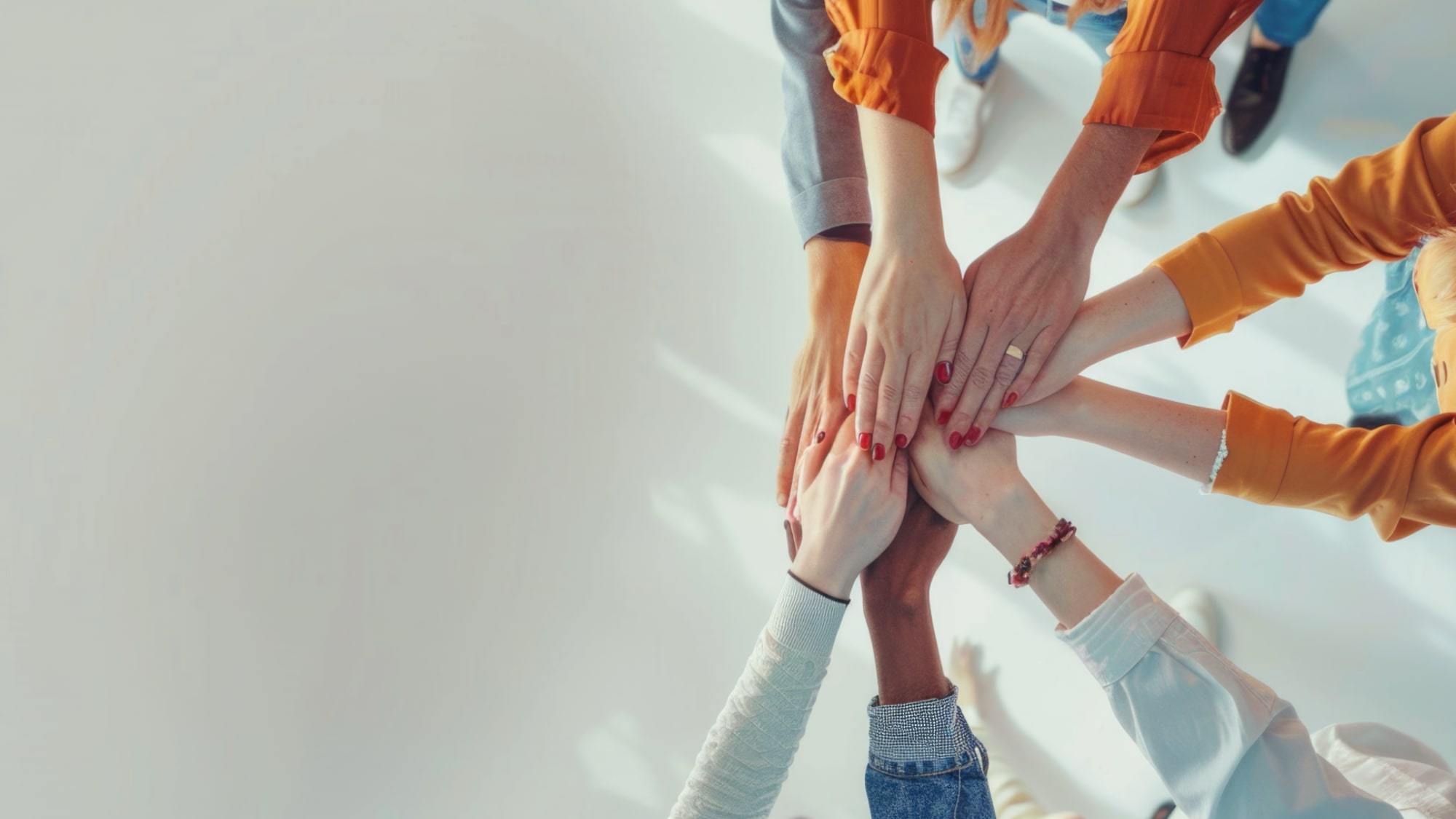A close-up view looking down at a stack of multiple hands gathered together, signifying teamwork and collaboration.