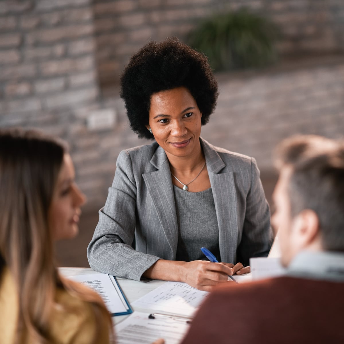 A young woman lawyer with short, curly, dark hair consulting with two clients.