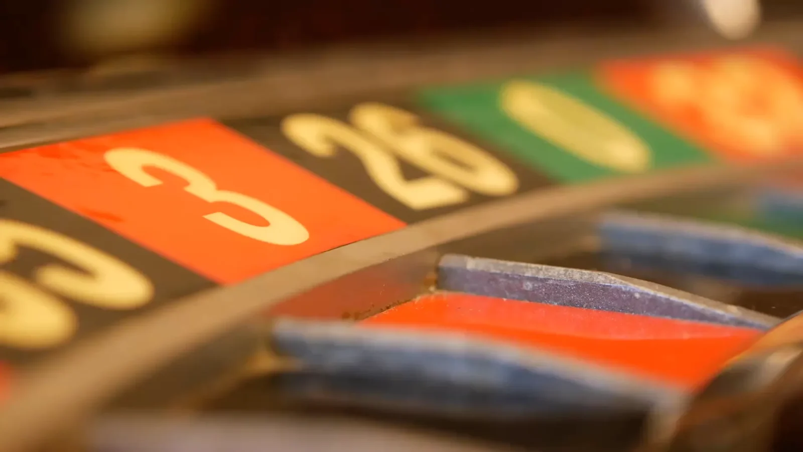 A macro close-up of a roulette wheel, sharply focused on the numbered slots '3' (red) and '26' (black). The image shows the detail of the metal dividers.