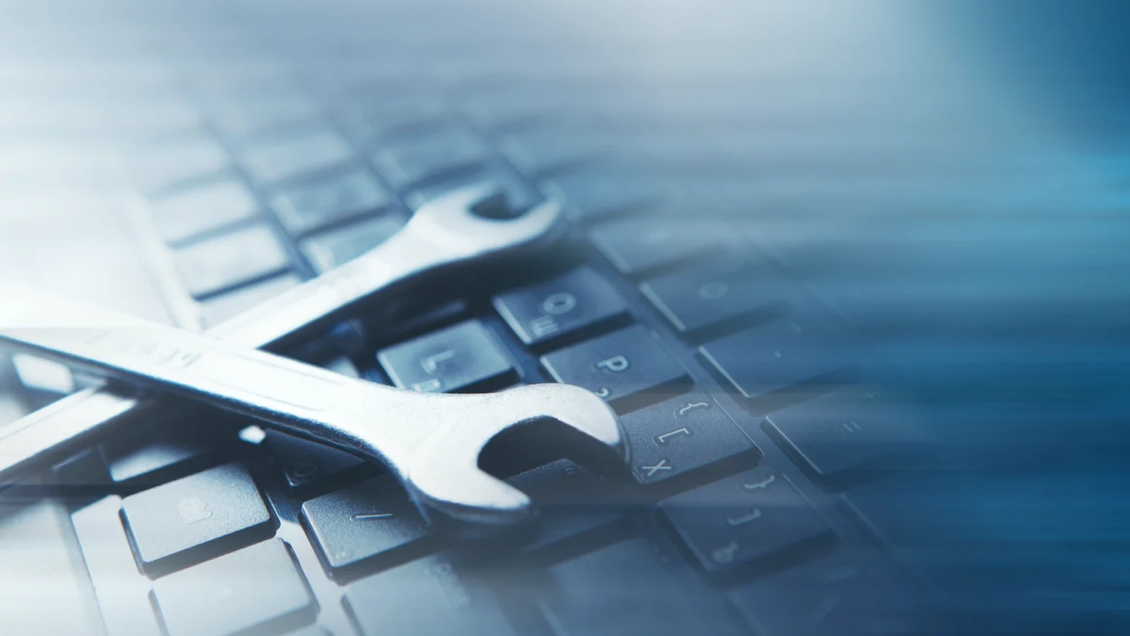 Two shiny, silver wrenches are crossed on the dark keys of a computer keyboard, suggesting computer maintenance and technical support.