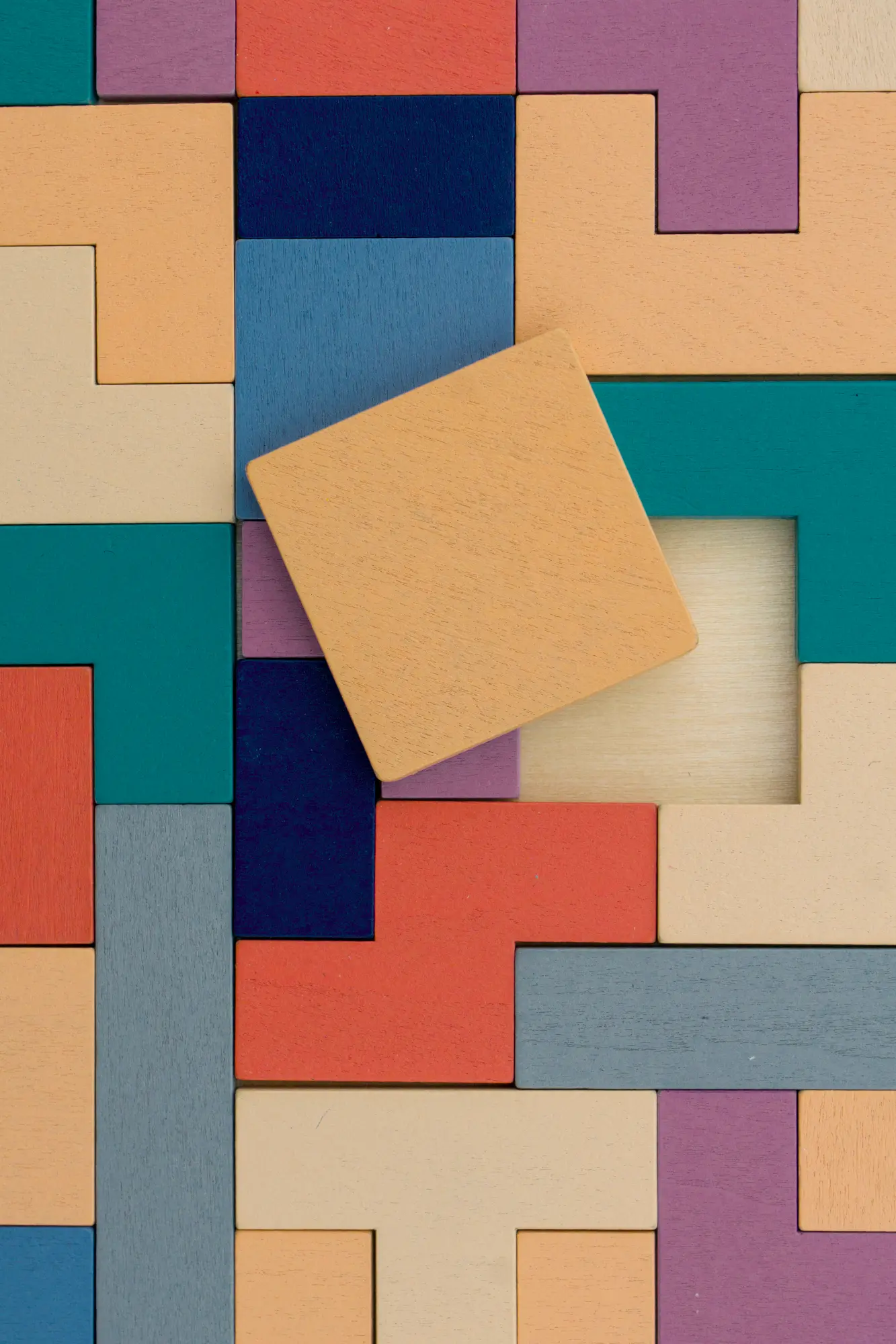 An array of colorful, interlocking wooden blocks with a light orange square piece tilted over the empty space it needs to fill.
